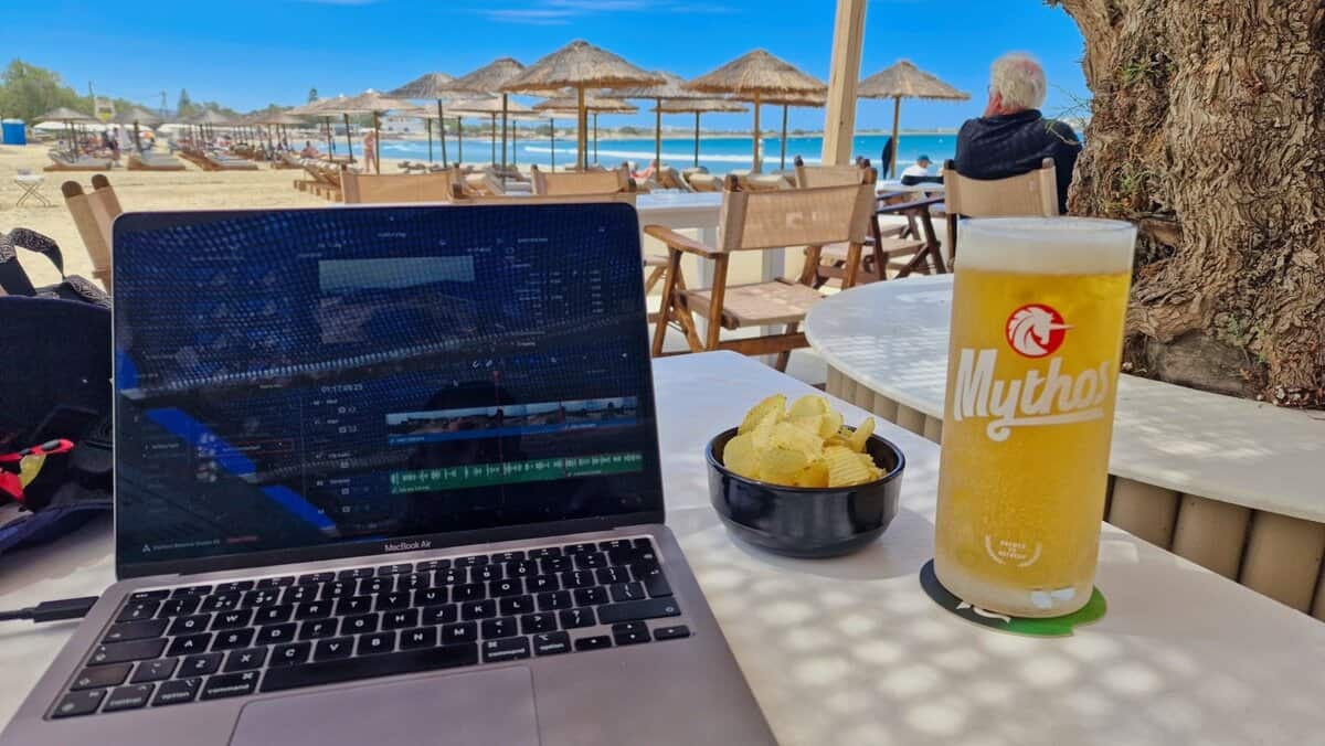 Laptop, Mythos, and crisps for work with Agios Georgios Beach backdrop on Naxos
